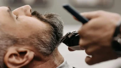حلاق يقص شعر رجل يظهر عليه الشيب (الشعر الأبيض) في صالون حلاقة، للتركيز على علاج الشعر الابيض والاهتمام به.
